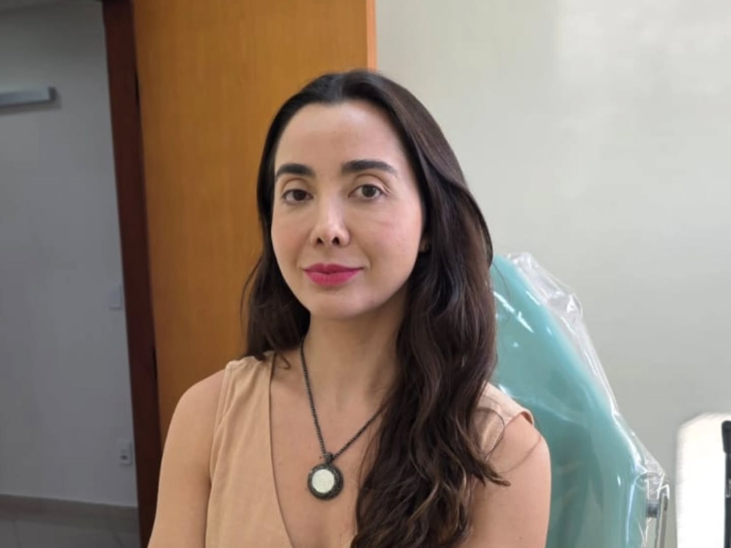 Mariana de blusa bege e colar, em um ambiente interno.